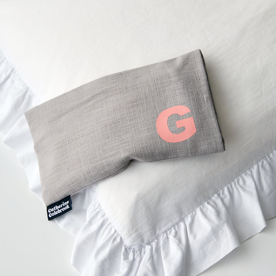 Catherine Colebrook grey linen eye pillow with salmon pink initial on the bottom right with optional lavender