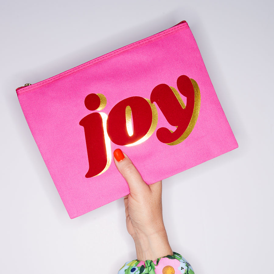 HAND HOLDING LARGE COTTON PINK PURSE WITH JOY WRITTEN IN RED & GOLD ON IT