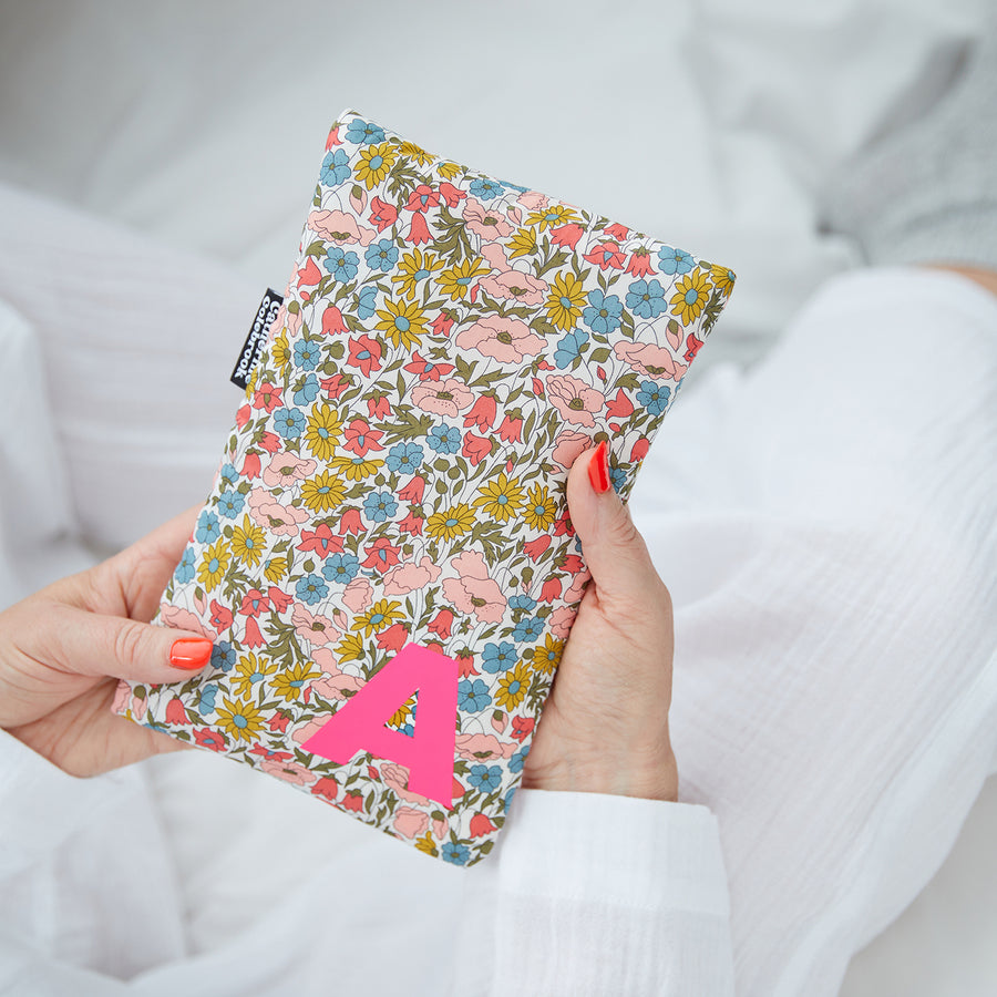 Hand holding cute hot water bottle in Floral Liberty print, personalised with a Neon Pink letter A.