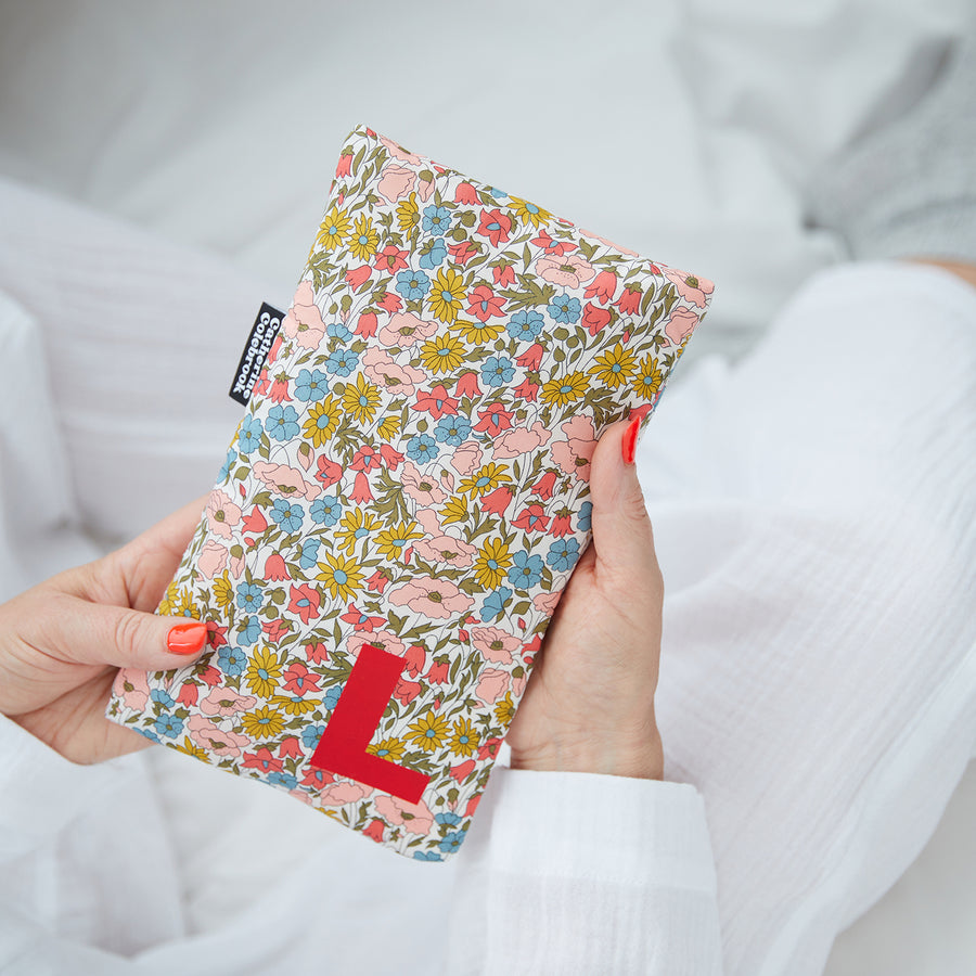 Hand holding cute hot water bottle in Floral Liberty print, personalised with a red letter L.