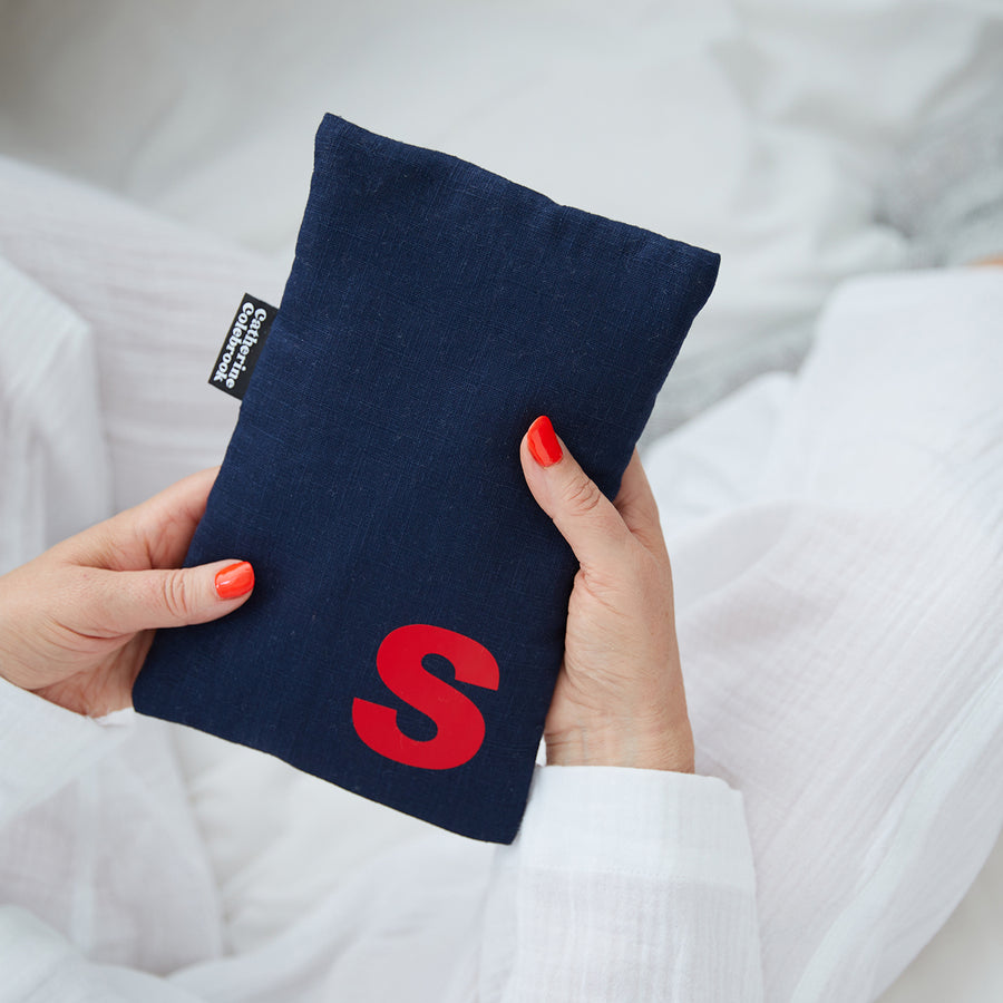Hand holding cute hot water bottle in Navy Linen, personalised with a red letter S.