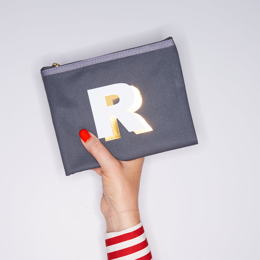 HAND HOLDING MEDIUM COTTON GREY PURSE WITH A WHITE LETTER R ON IT