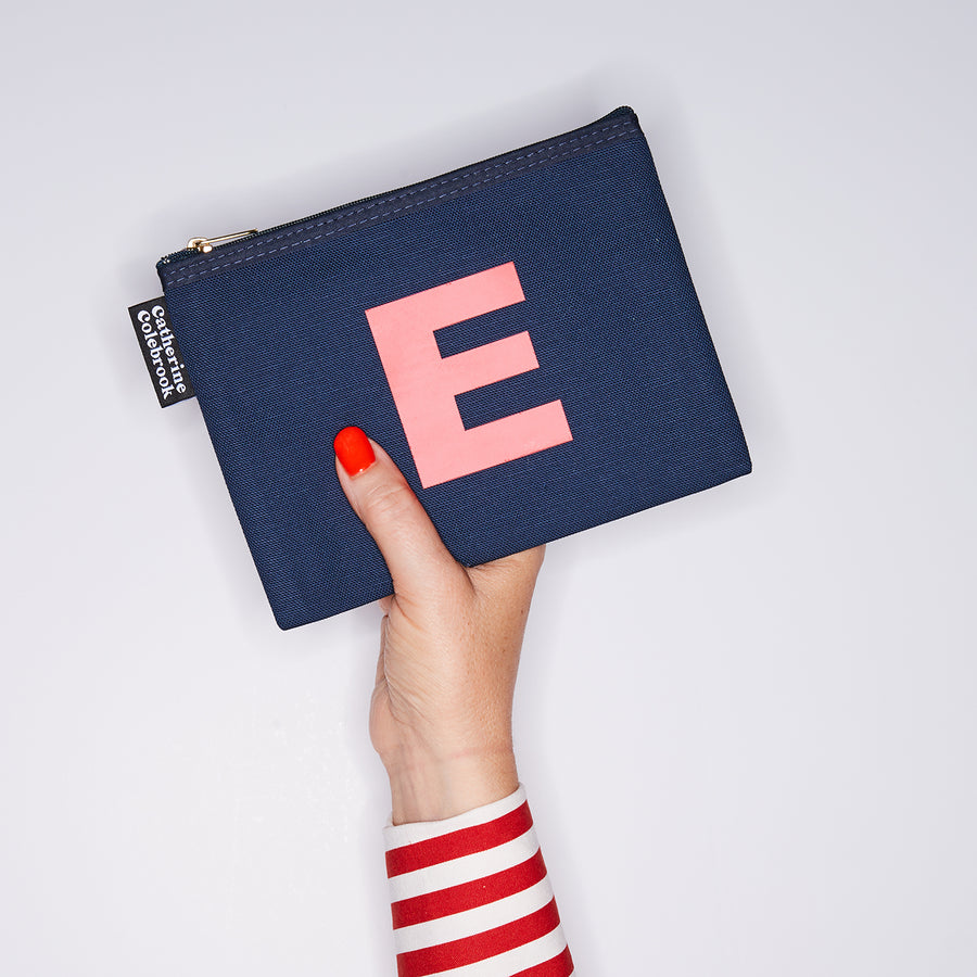 HAND HOLDING MEDIUM COTTON NAVY PURSE WITH A SALMON PINK LETTER E ON IT