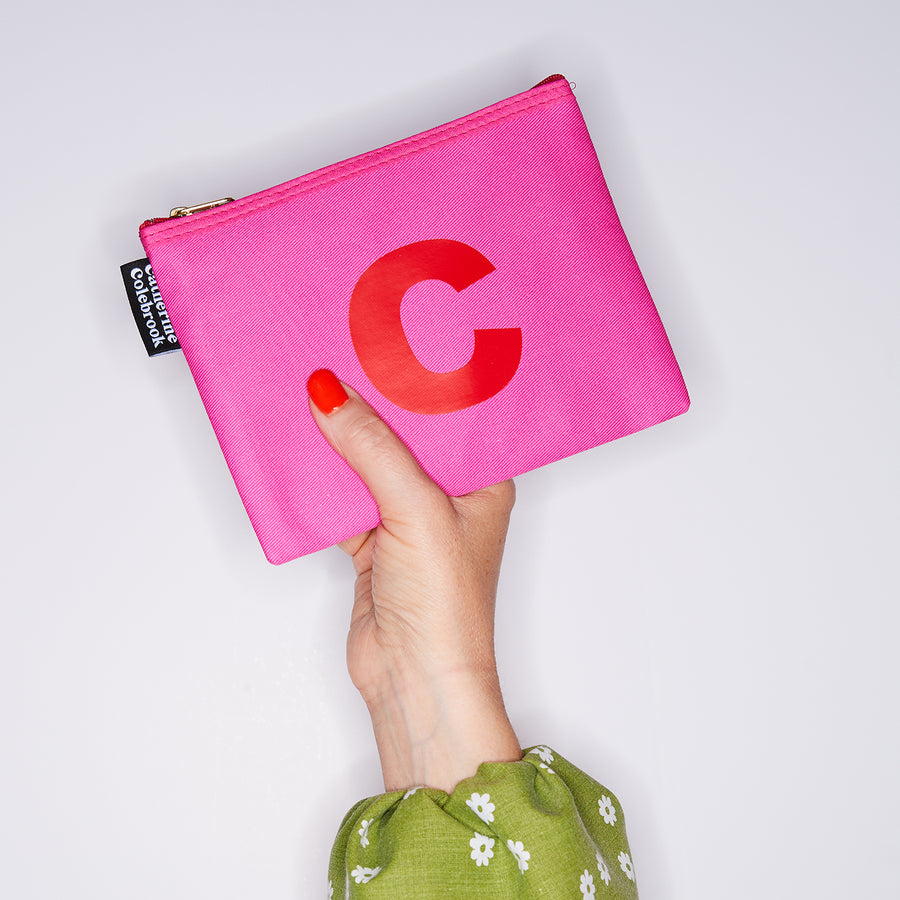HAND HOLDING MEDIUM COTTON PINK PURSE WITH A RED LETTER C ON IT