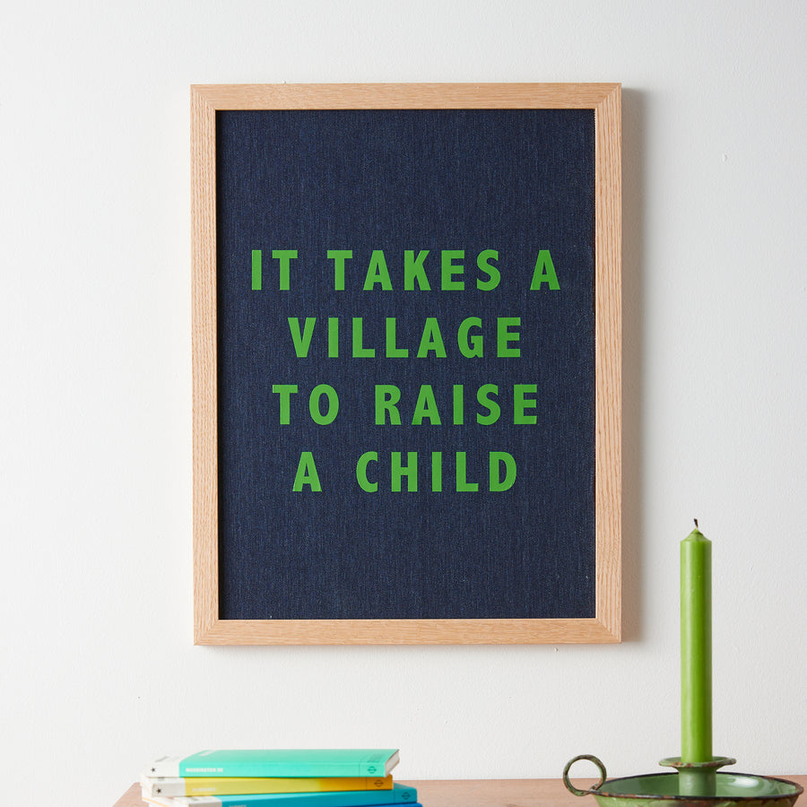 Catherine Colebrook framed denim quote picture, ‘It Takes a Village to Raise a Child' in denim with green text, in an oak frame