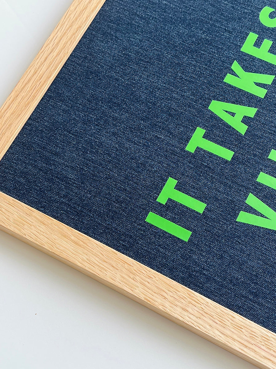 Catherine Colebrook framed denim quote picture, ‘It Takes a Village to Raise a Child' in denim with green text, in an oak frame - close up