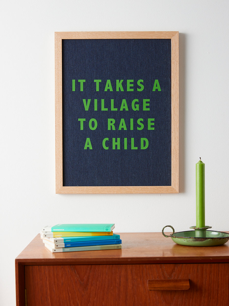 Catherine Colebrook framed denim quote picture, ‘It Takes a Village to Raise a Child' in denim with green text, in an oak frame