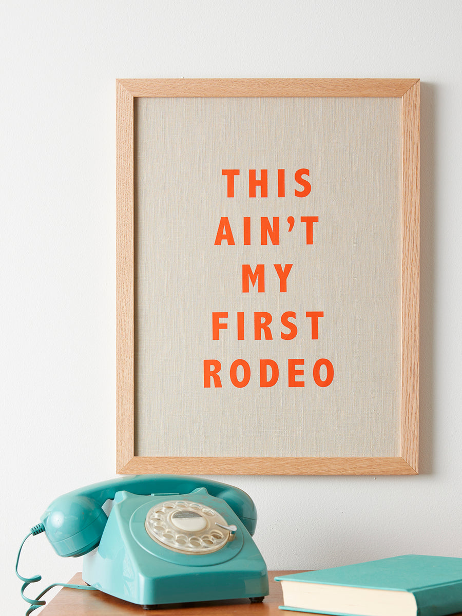 Catherine Colebrook framed linen quote picture, ’This Ain’t My First Rodeo' in natural linen with orange text, in an oak frame