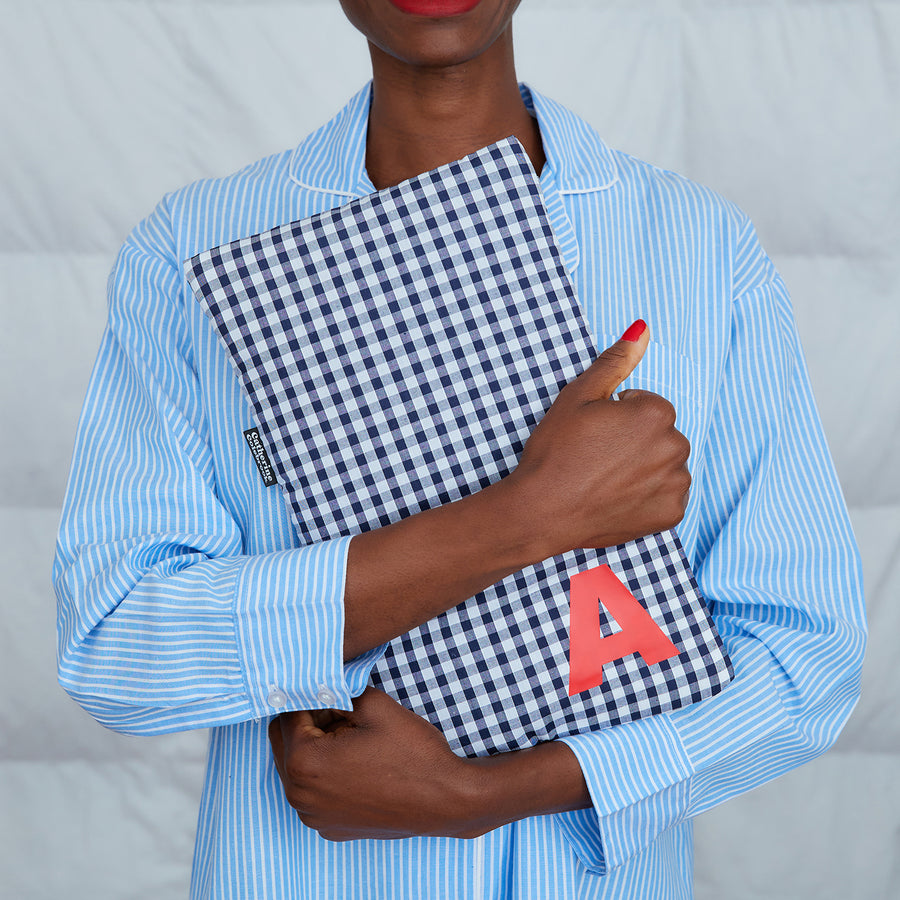 woman hugging navy gingham hot water bottle, personalised with red A