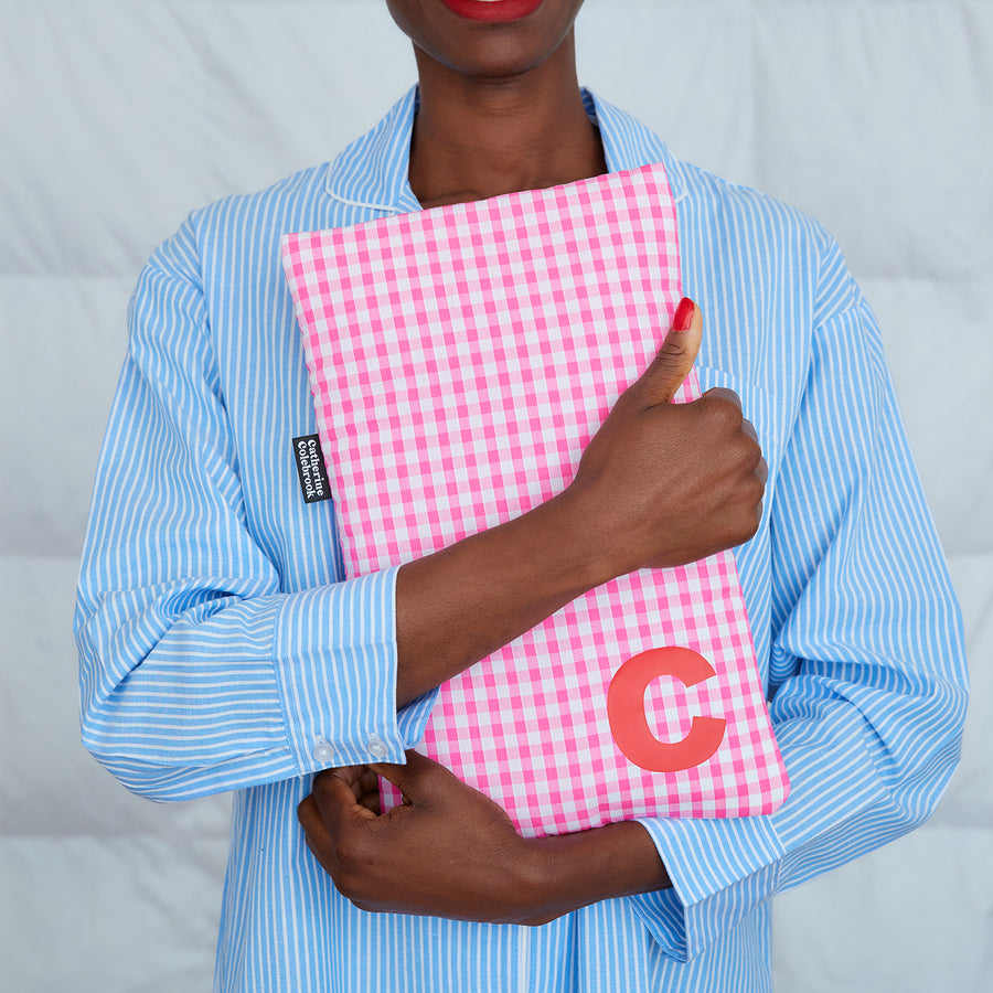 woman hugging pink gingham hot water bottle, personalised with red C