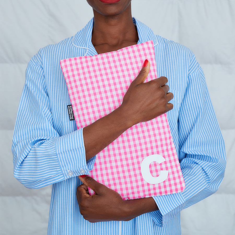 woman hugging pink gingham hot water bottle, personalised with white C