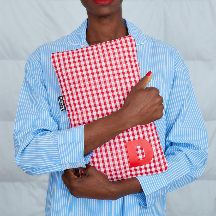 woman hugging red gingham hot water bottle, personalised with red D