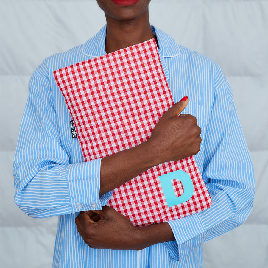 woman hugging red gingham hot water bottle, personalised with turquoise D