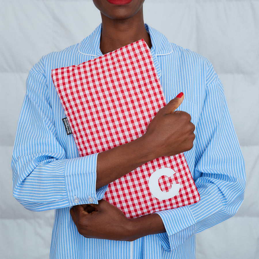 woman hugging red gingham hot water bottle, personalised with white C