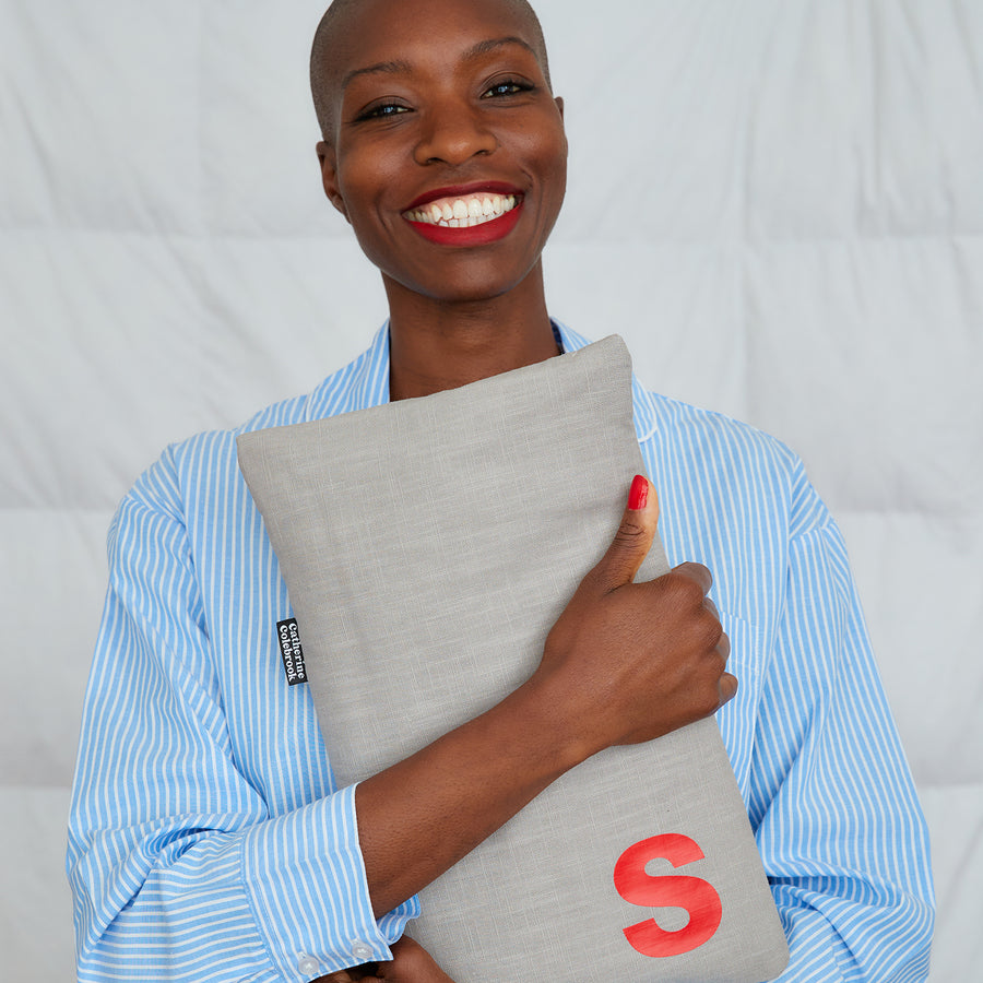 smiling woman hugging grey linen hot water bottle, personalised with red S