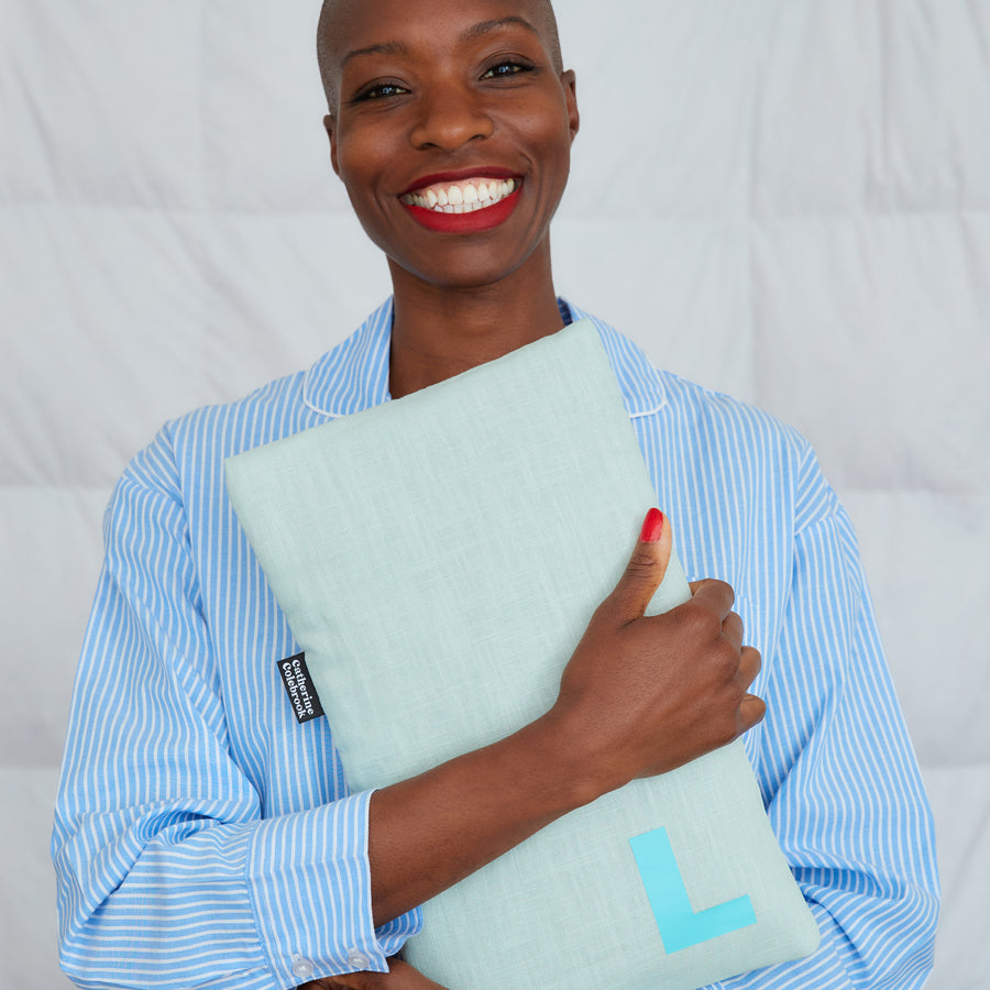 smiling woman hugging mint linen hot water bottle, personalised with turquoise L
