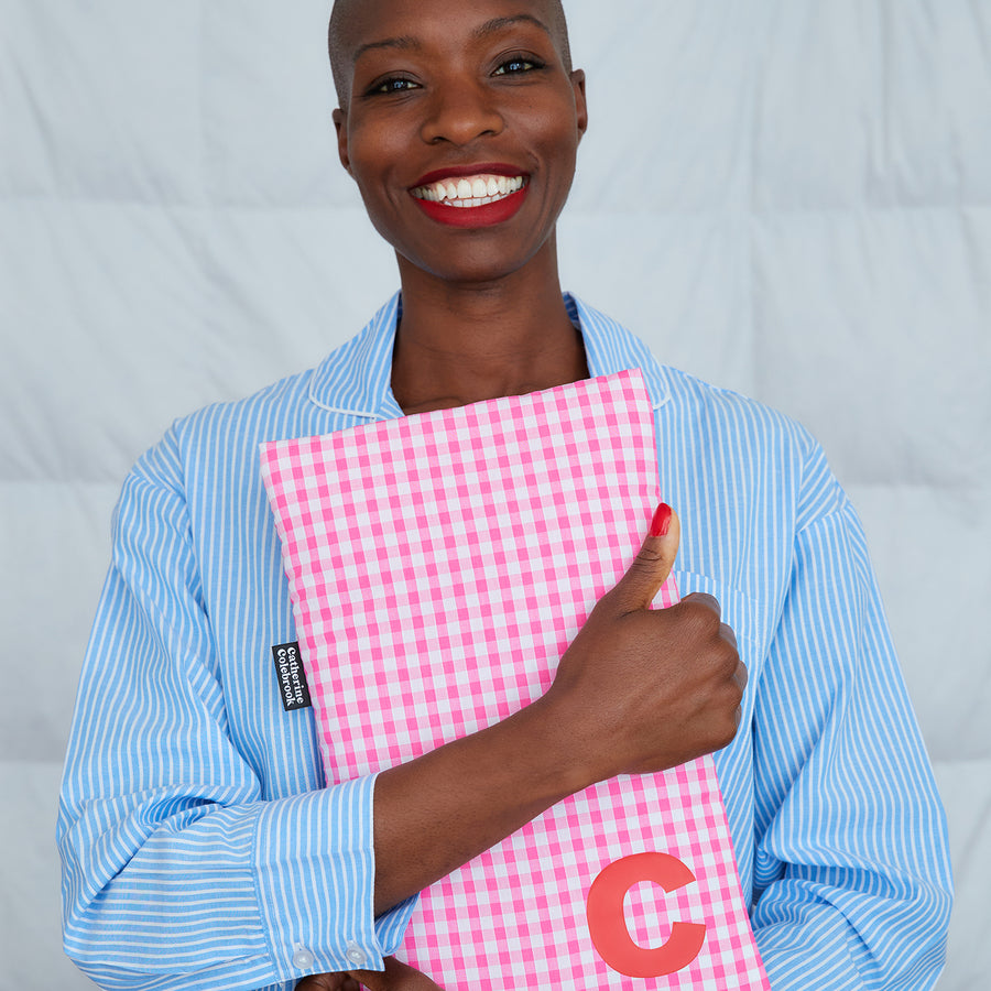 smiling woman hugging pink gingham hot water bottle, personalised with red C