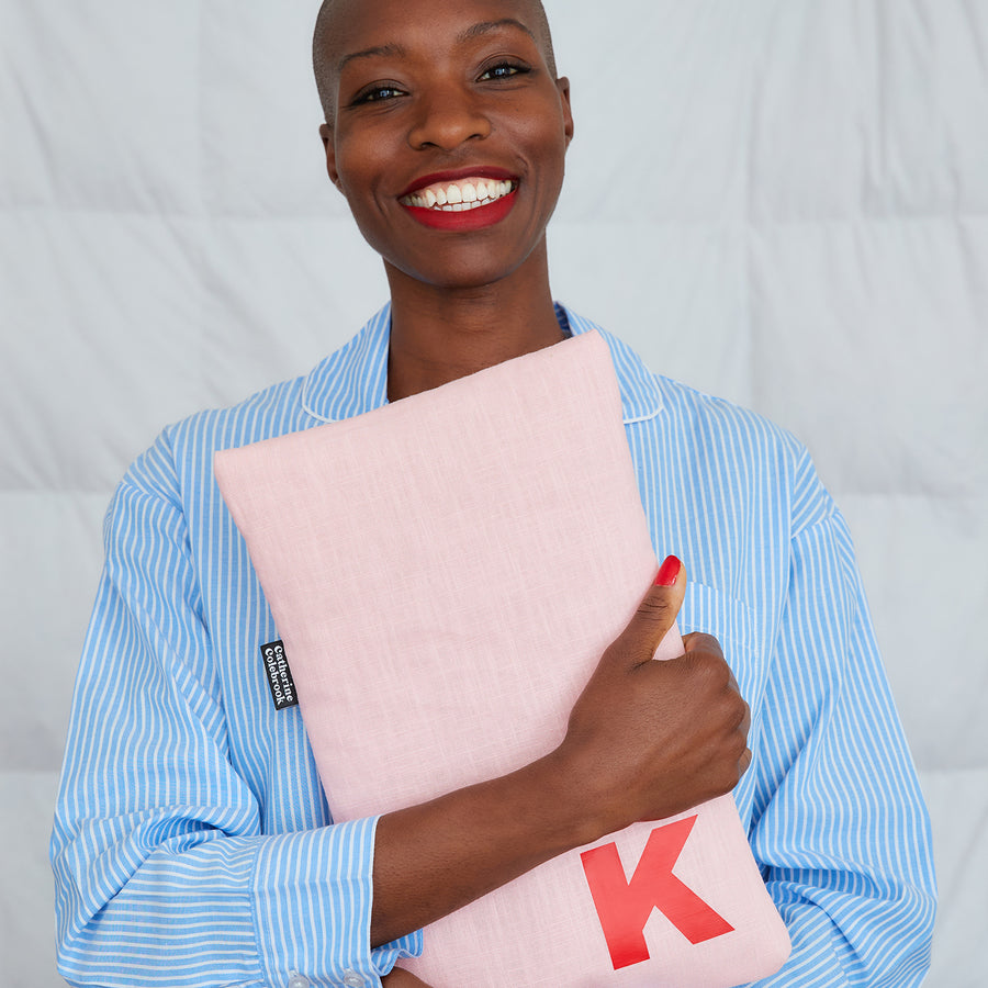 smiling woman hugging pink linen hot water bottle, personalised with red K