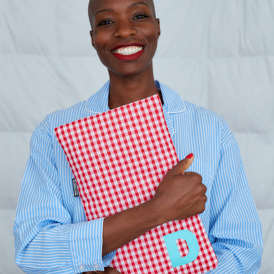 smiling woman hugging red gingham hot water bottle, personalised with turquoise D