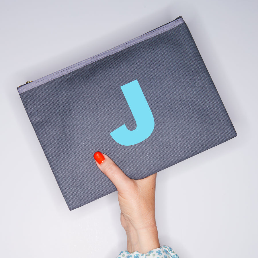 HAND HOLDING LARGE COTTON GREY PURSE WITH AN TURQUOISE LETTER J ON IT