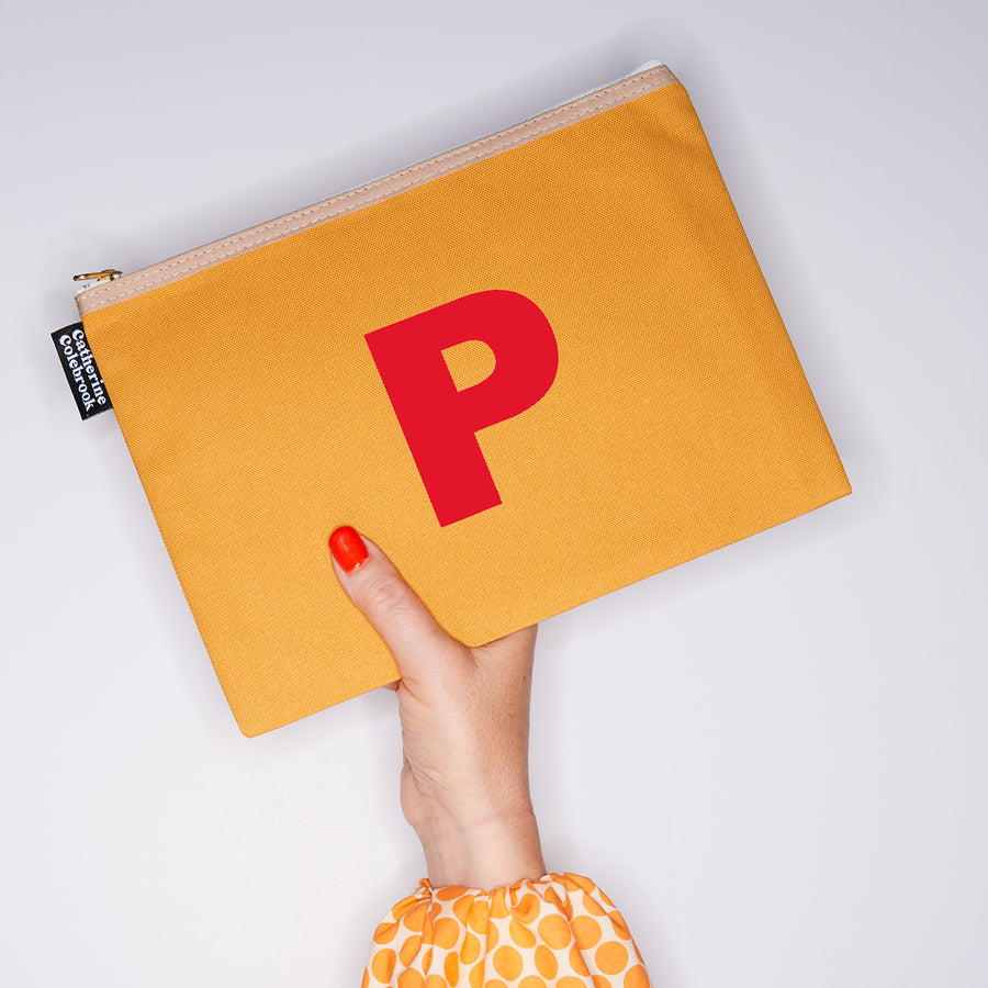 HAND HOLDING LARGE COTTON MUSTARD PURSE WITH AN RED LETTER P ON IT