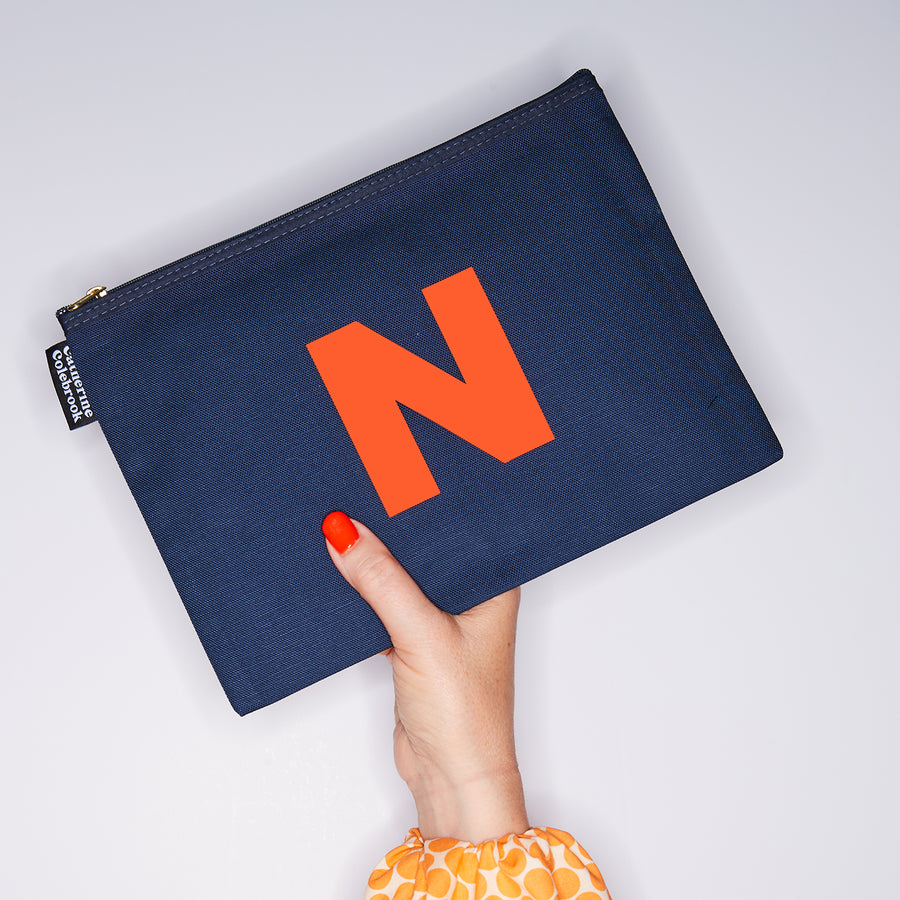 HAND HOLDING LARGE COTTON NAVY PURSE WITH AN ORANGE LETTER N ON IT