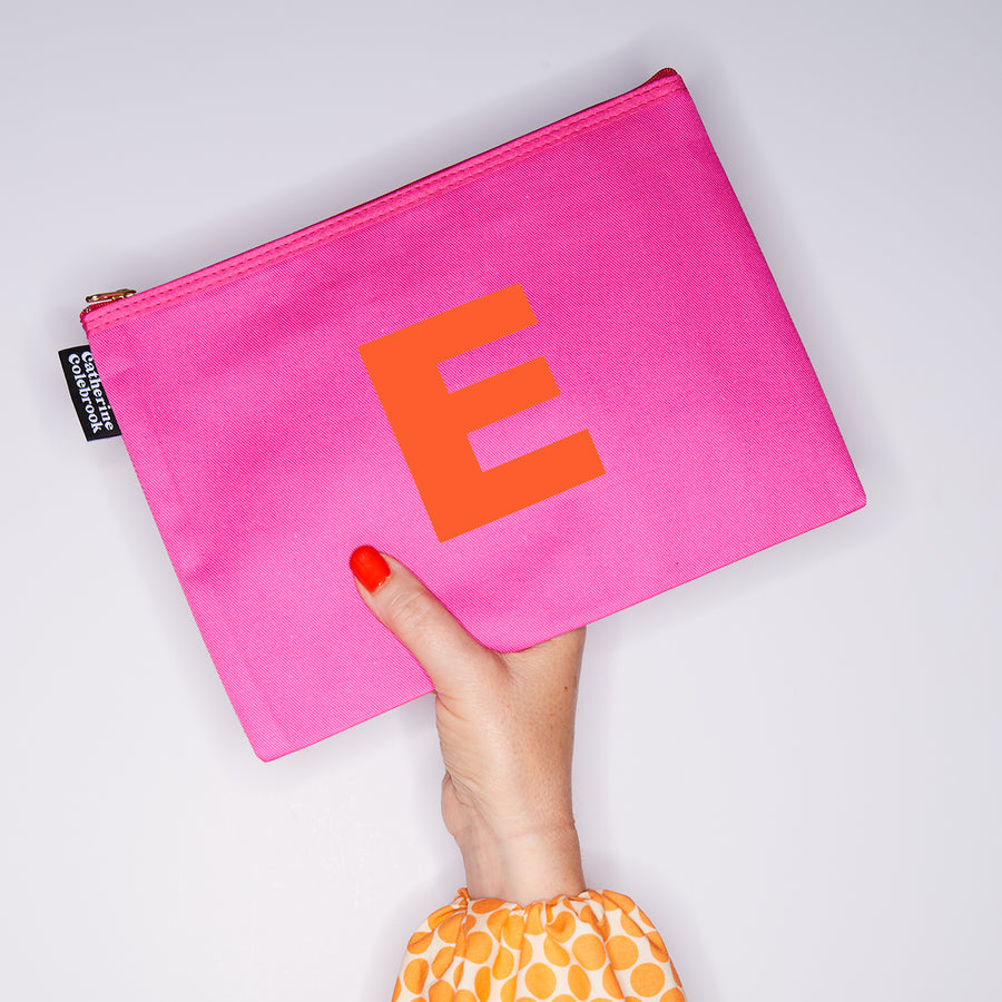 HAND HOLDING LARGE COTTON PINK PURSE WITH AN ORANGE LETTER E ON IT