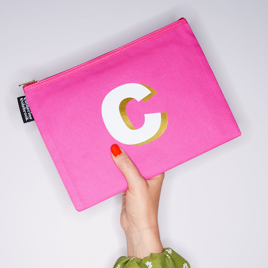 HAND HOLDING LARGE COTTON PINK PURSE WITH A WHITE LETTER C ON IT