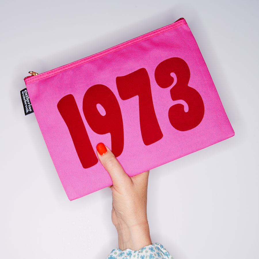 HAND HOLDING PINK COTTON YEAR PURSE WITH A RED 1973 ON IT
