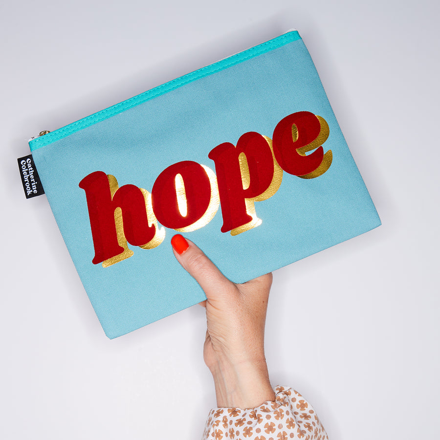 HAND HOLDING LARGE COTTON TURQUOISE PURSE WITH HOPE WRITTEN IN RED & GOLD ON IT