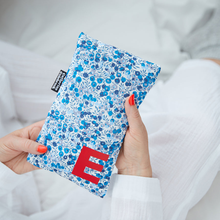 Hand holding cute hot water bottle in Blue Liberty print, personalised with a red letter E.