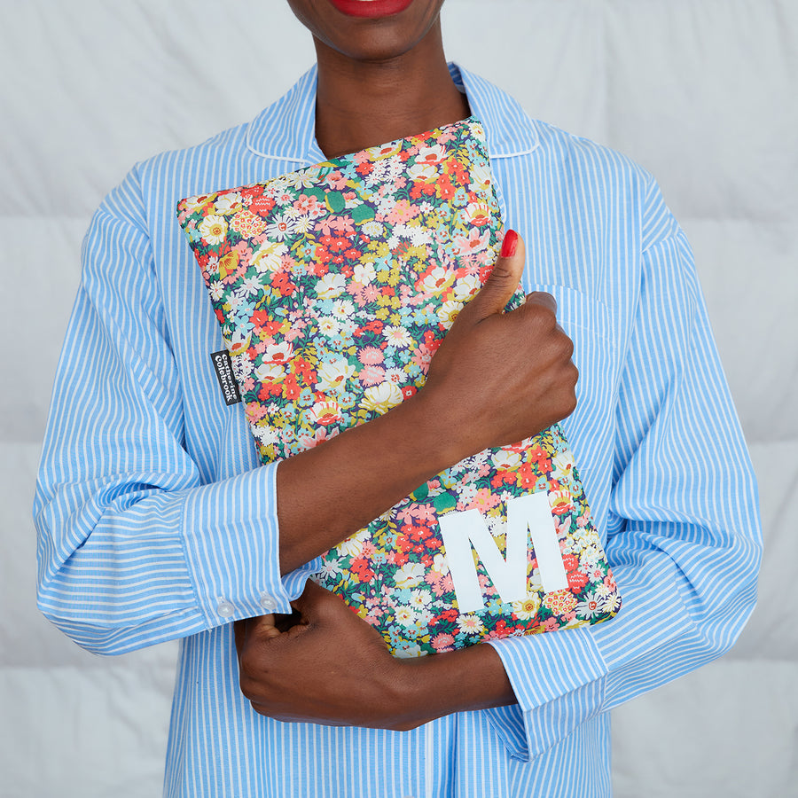 woman hugging green/pink Liberty print hot water bottle, personalised with white M