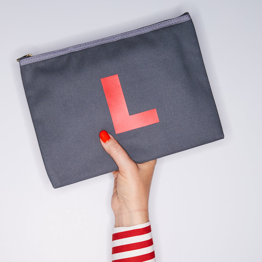 HAND HOLDING LARGE COTTON GREY PURSE WITH AN RED LETTER L ON IT