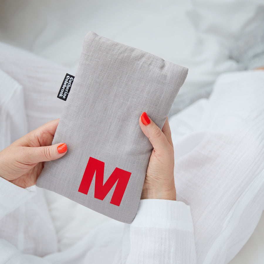 Hand holding cute hot water bottle in Grey Linen, personalised with a red letter M.