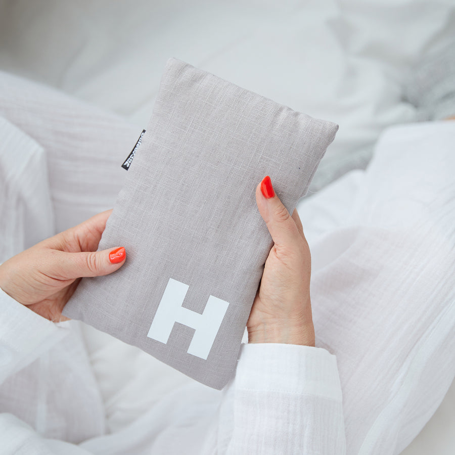 Hand holding cute hot water bottle in Grey Linen, personalised with a white letter H.