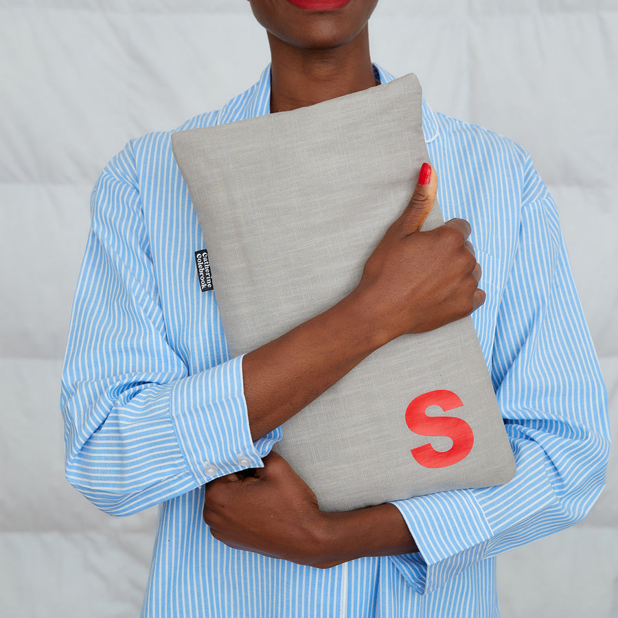 woman hugging grey linen hot water bottle, personalised with red S