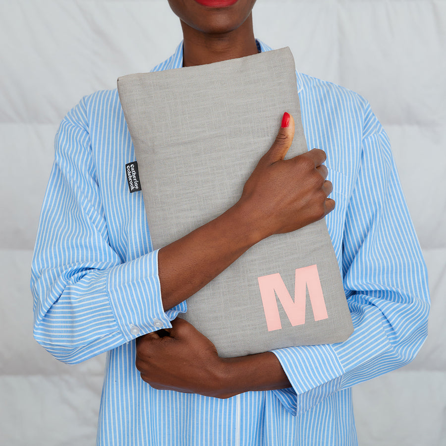 woman hugging grey linen hot water bottle, personalised with pink M