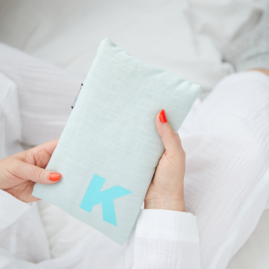 Hand holding cute hot water bottle in Mint Linen, personalised with a turquoise letter K.