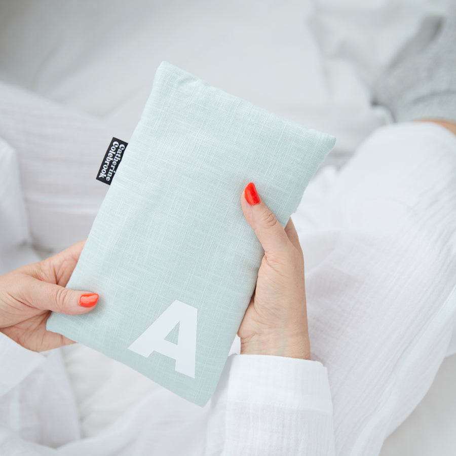 Hand holding cute hot water bottle in Mint Linen, personalised with a white letter A.