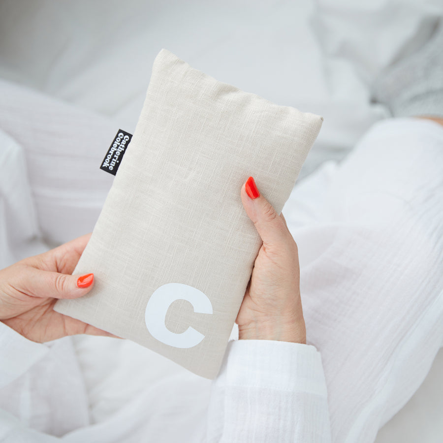 Hand holding cute hot water bottle in Natural Linen, personalised with a white letter C.