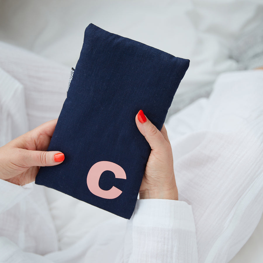 Hand holding cute hot water bottle in Navy Linen, personalised with a salmon letter C.