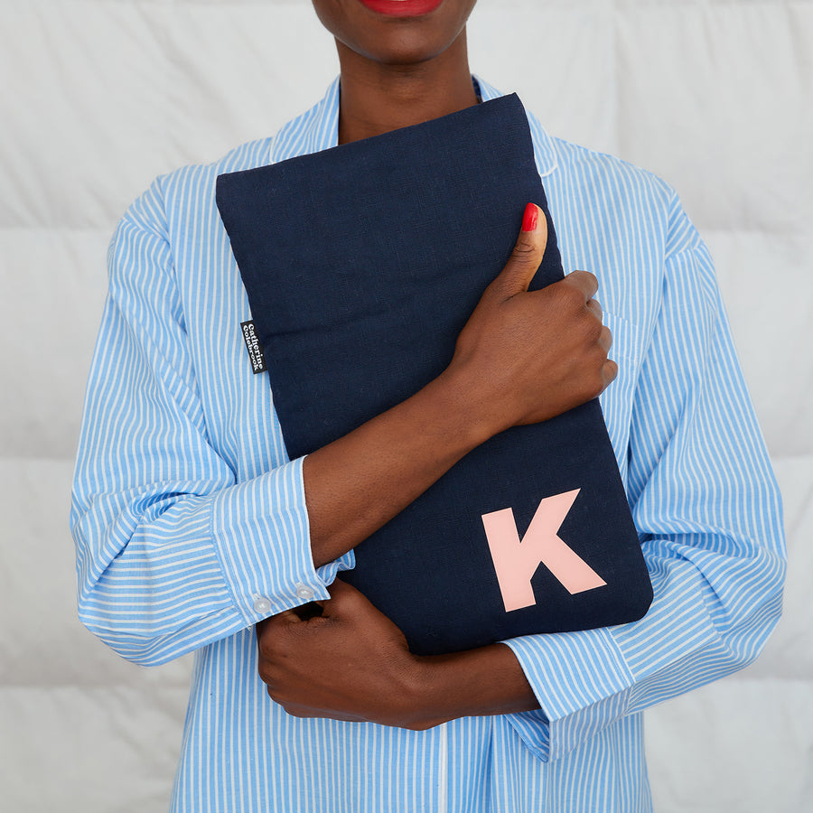 woman hugging navy linen hot water bottle, personalised with pink K