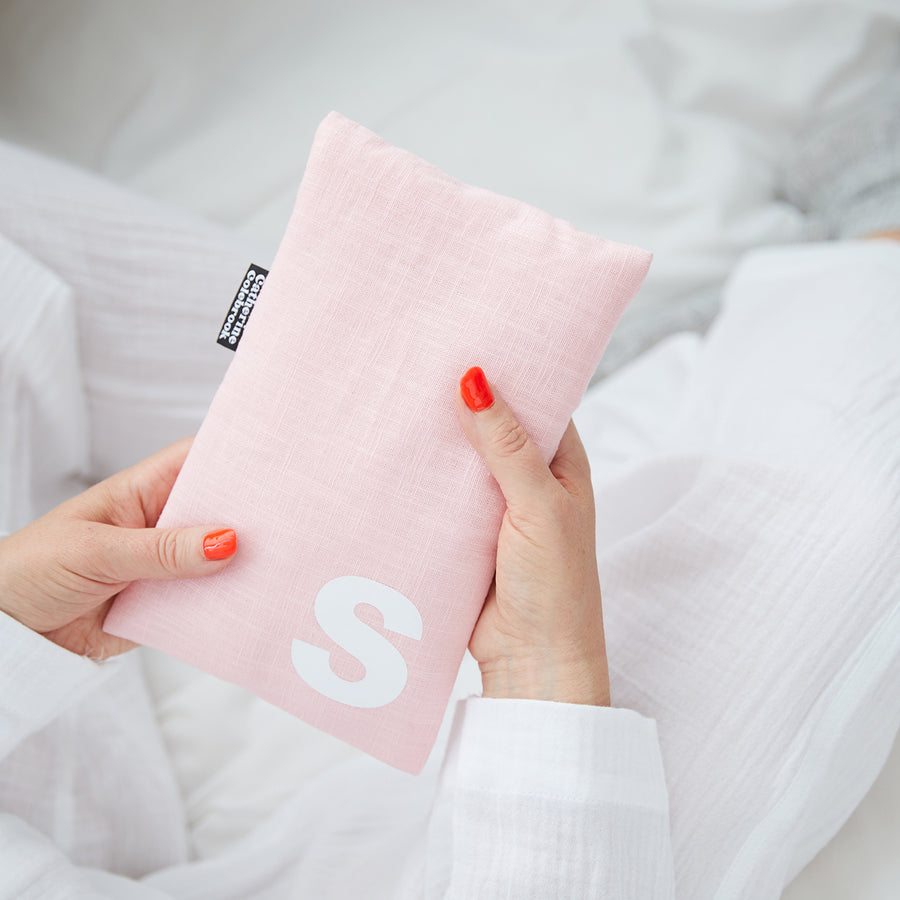 Hand holding cute hot water bottle in Pink Linen, personalised with a white letter S.