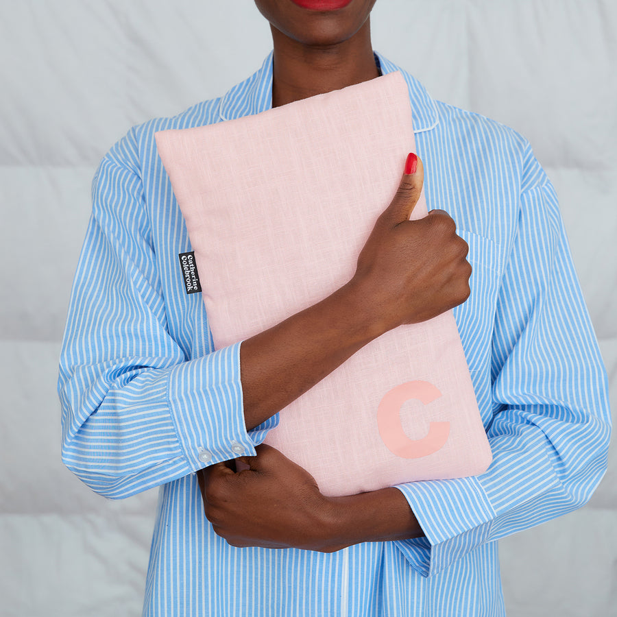 woman hugging pink linen hot water bottle, personalised with pink C
