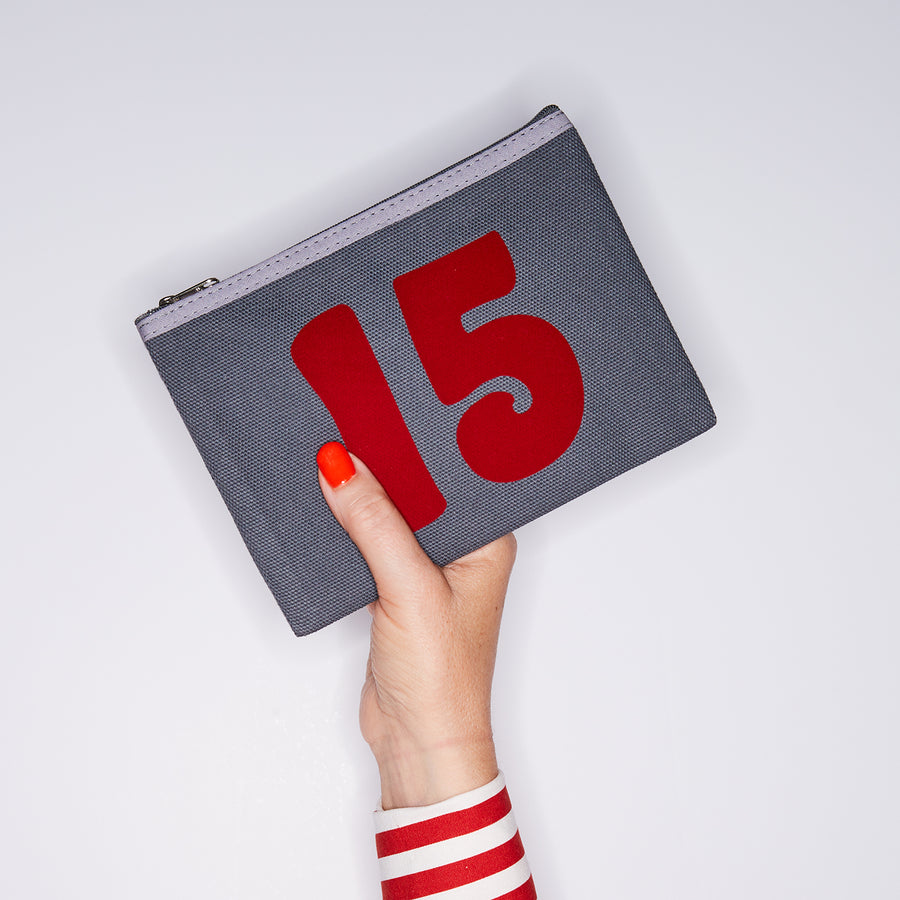 HAND HOLDING GREY COTTON PURSE WITH A RED NO 15 ON IT