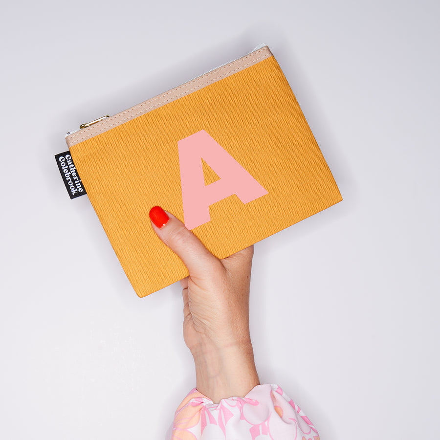 HAND HOLDING MEDIUM COTTON MUSTARD PURSE WITH A SALMON PINK LETTER A ON IT