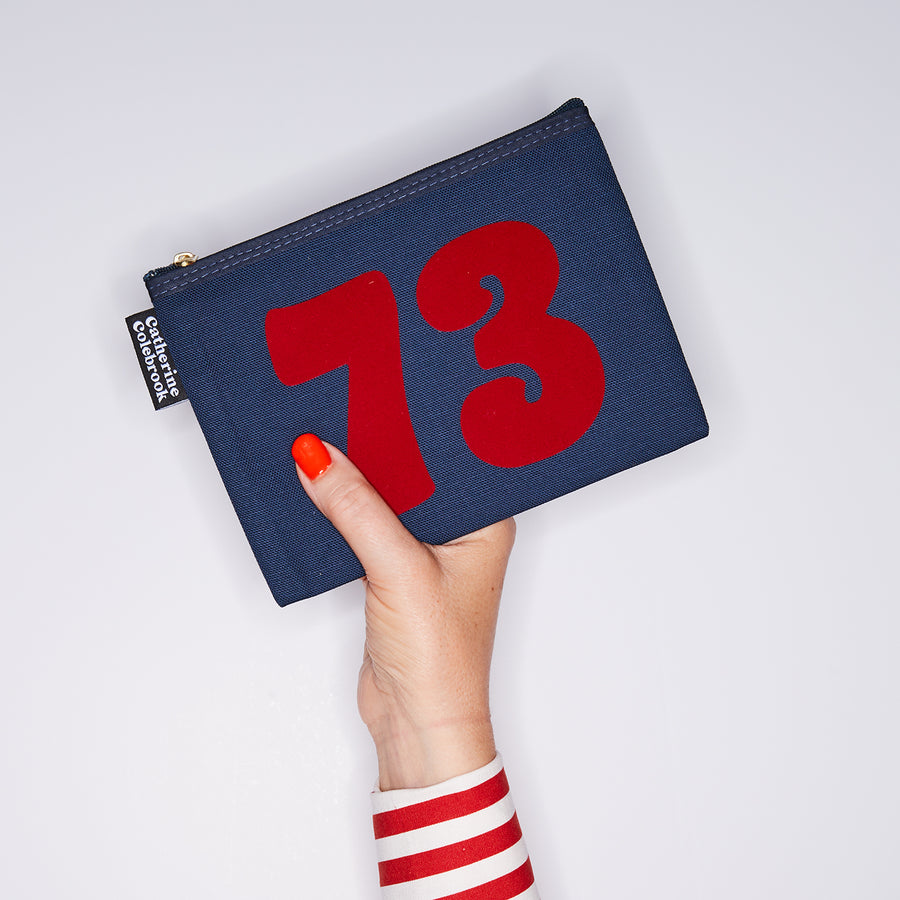 HAND HOLDING NAVY COTTON PURSE WITH A RED NO 73 ON IT