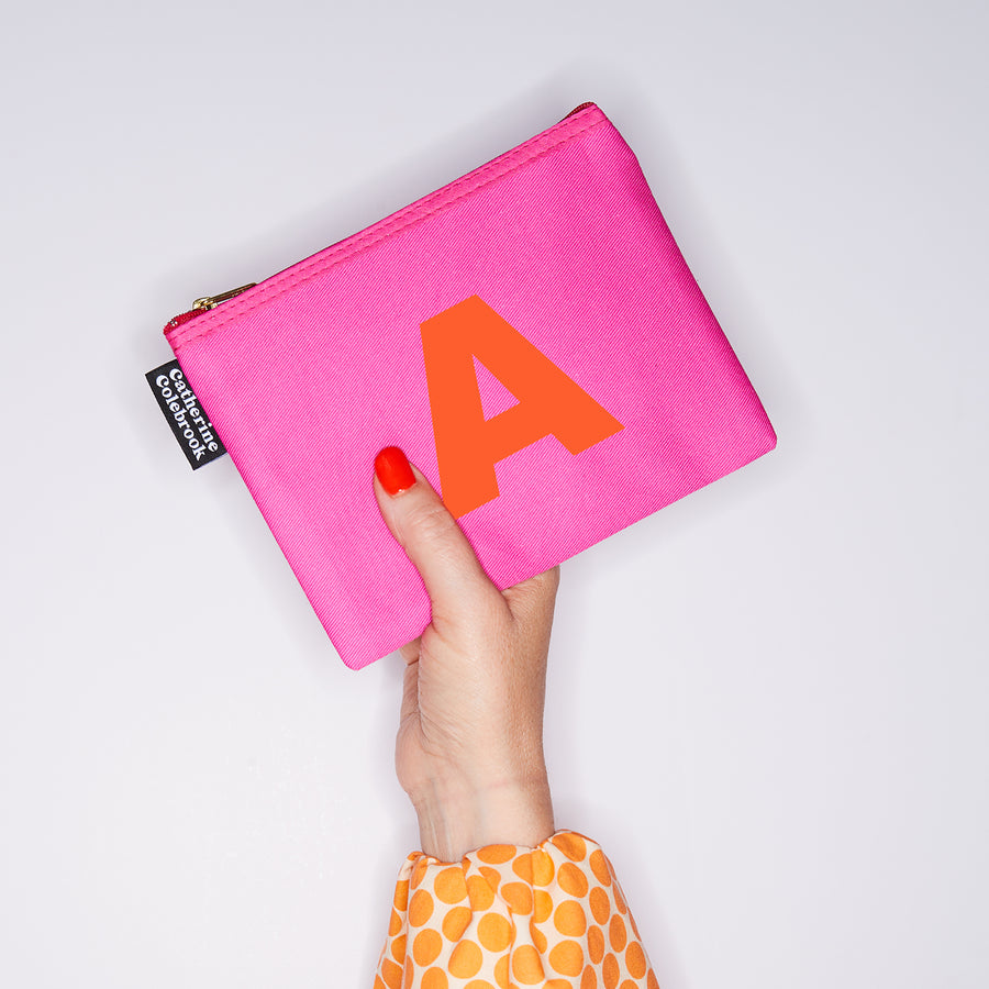 HAND HOLDING MEDIUM COTTON PINK PURSE WITH AN ORANGE LETTER A ON IT