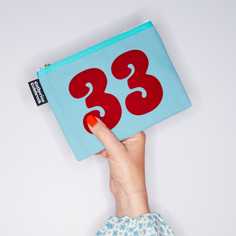 HAND HOLDING TURQUOISE COTTON PURSE WITH A RED NO 33 ON IT