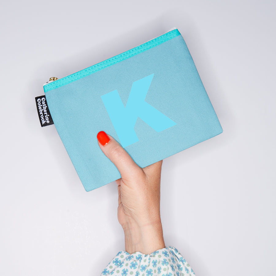 HAND HOLDING MEDIUM COTTON TURQUOISE PURSE WITH A TURQUOISE LETTER K ON IT